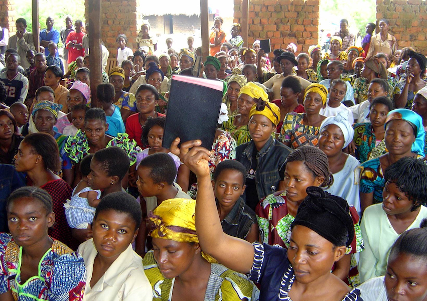 Students assembled in a common area; one female student holds a single Bible aloft