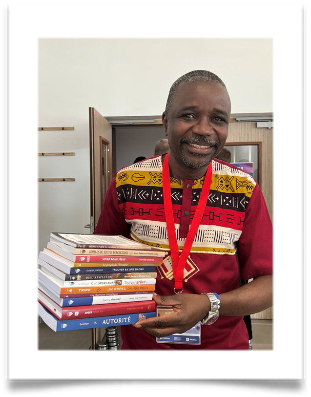 A pastor smiles while holding a stack of books gifted to him.